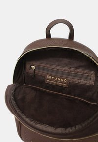 Zaino in pelle marrone con superficie strutturata, zip dorata e interno in tessuto morbido. Presenta una tasca frontale con zip e branding all'interno.