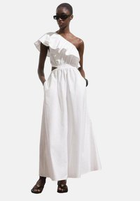Robe blanche à épaule unique avec un col à volants, taille élastique et poches latérales. Fabriquée dans un tissu léger, elle présente une silhouette fluide.