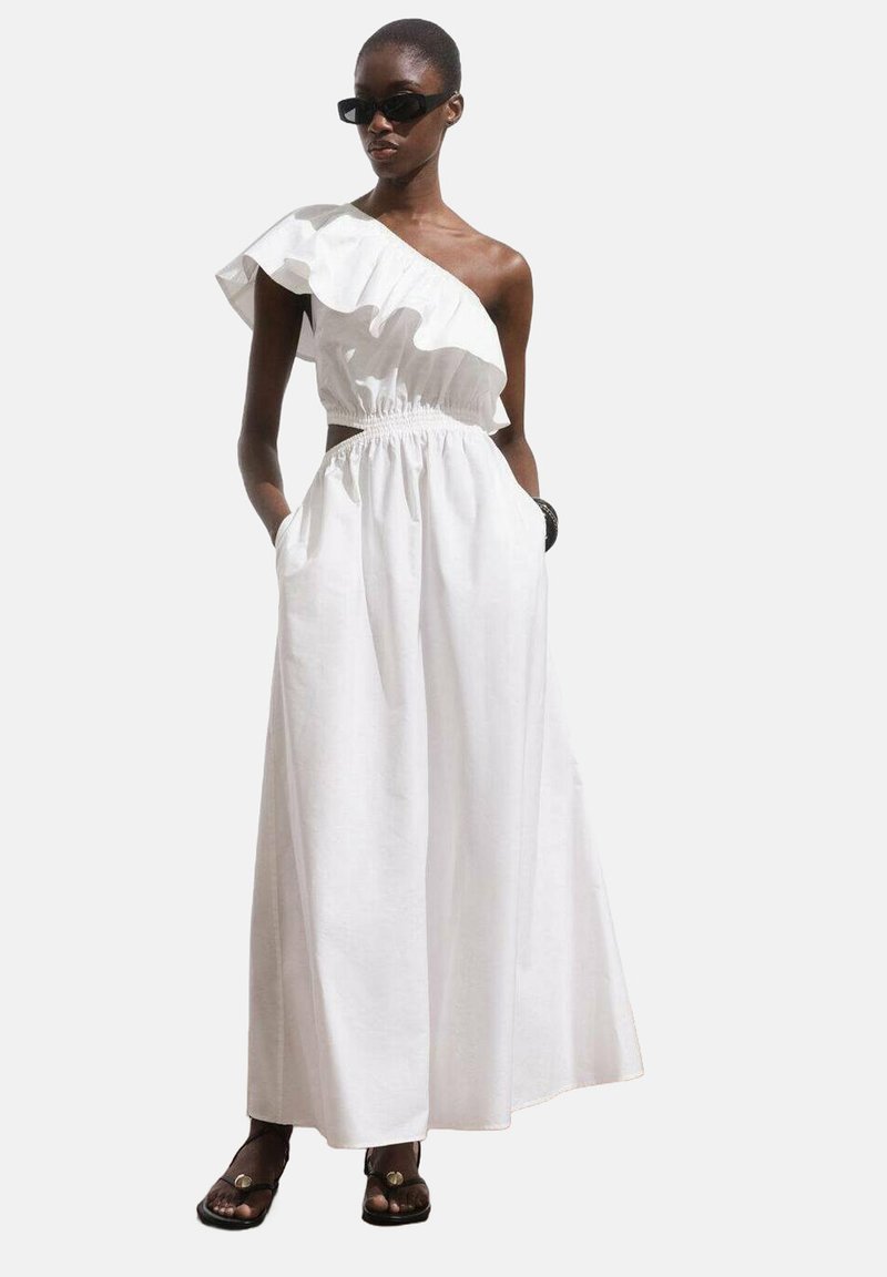 Robe blanche à épaule unique avec un col à volants, taille élastique et poches latérales. Fabriquée dans un tissu léger, elle présente une silhouette fluide.