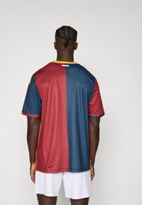 Kortærmet fodboldtrøje med et delt design i bordeaux og mørkeblå, med en ribbet tekstur og en gul krave.