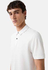 Witte polo shirt met een klassieke kraag, korte mouwen en een geweven stof. Beschikt over een subtiel geborduurd logo en zwarte knopen.