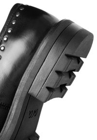 Gros plan d'un talon de chaussure en cuir noir avec des clous métalliques le long du bord et une semelle en caoutchouc texturée épaisse avec des motifs profonds.