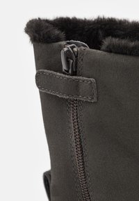 Botine din suede gri închis cu închidere prin fermoar și captuseală moale din blană neagră în partea de sus. Detalii cusute și o curea laterală sunt vizibile.
