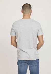 T-shirt gris à manches courtes en coton avec un col rond, porté avec un jean bleu, affichant un design simple et épuré.