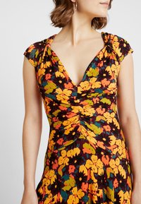 Kwiatowa sukienka z głębokim dekoltem w kształcie litery V, krótkimi rękawkami, marszczeniami na biu�ście oraz kolorowym wzorem w odcieniach żółtego, pomarańczowego i zielonego na ciemnym tle.