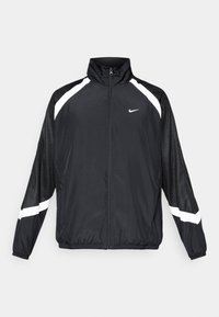 Veste de sport noire Nike avec fermeture éclair intégrale devant, bandes blanches sur les épaules et les manches, et poignets ainsi que ourlet élastiques.