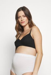 Sutiã de maternidade preto com rendas e alças ajustáveis, combinado com cuecas brancas de cintura alta. Tecido macio e elástico para conforto.