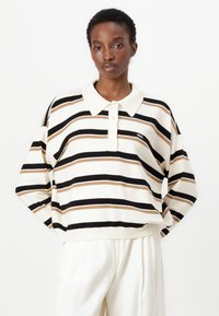 Kremfarget oversized polo-skjorte med horisontale svarte, brune og beige striper. Har knapper foran og ribbestrikket nederkant. Myk tekstur.