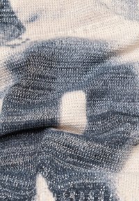 Gestrickter Pulloverstoff mit einer Mischung aus hellen Creme- und dunklen Grautönen; verfügt über eine weiche Textur und einen subtilen Glanz durch metallische Fäden.