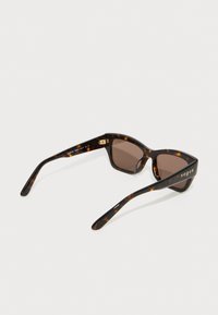 Ochelari de soare cu un design în formă de ochi de pisică, cu ramă din scoică, lentile de culoare maro și brandul "vogue" aurit pe partea laterală. Finisaj neted și lucios.