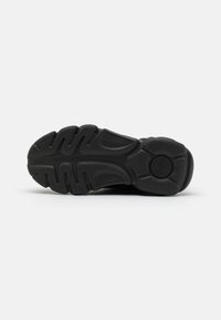 Black rubber sole with a textured grip pattern. Features curved grooves and circular accents, designed for traction and support.