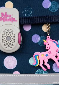 Tissu bleu marine avec des pois colorés, comportant un dispositif McNeil blanc et un charme licorne rose avec une crinière multicolore et des accents en forme d'étoile.