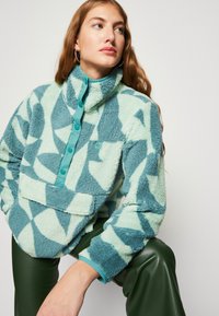 Fluffy fleece trui in mintgroen en teal geometrische patronen, met een hoge kraag, knoopsluiting en een voorzak.