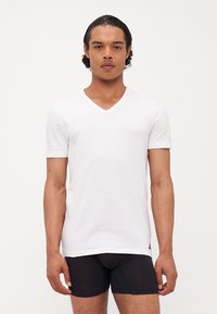 Weißes kurzärmeliges V-Ausschnitt-T-Shirt aus glattem Stoff, mit figurbetontem Design und subtilen Logo-Details am Saum.