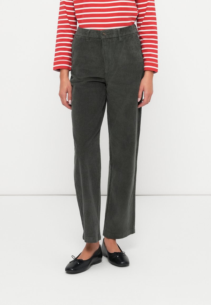 Green corduroy trousers with a straight-leg design, featuring a button closure and pockets. Paired with black flat shoes. Red striped top.