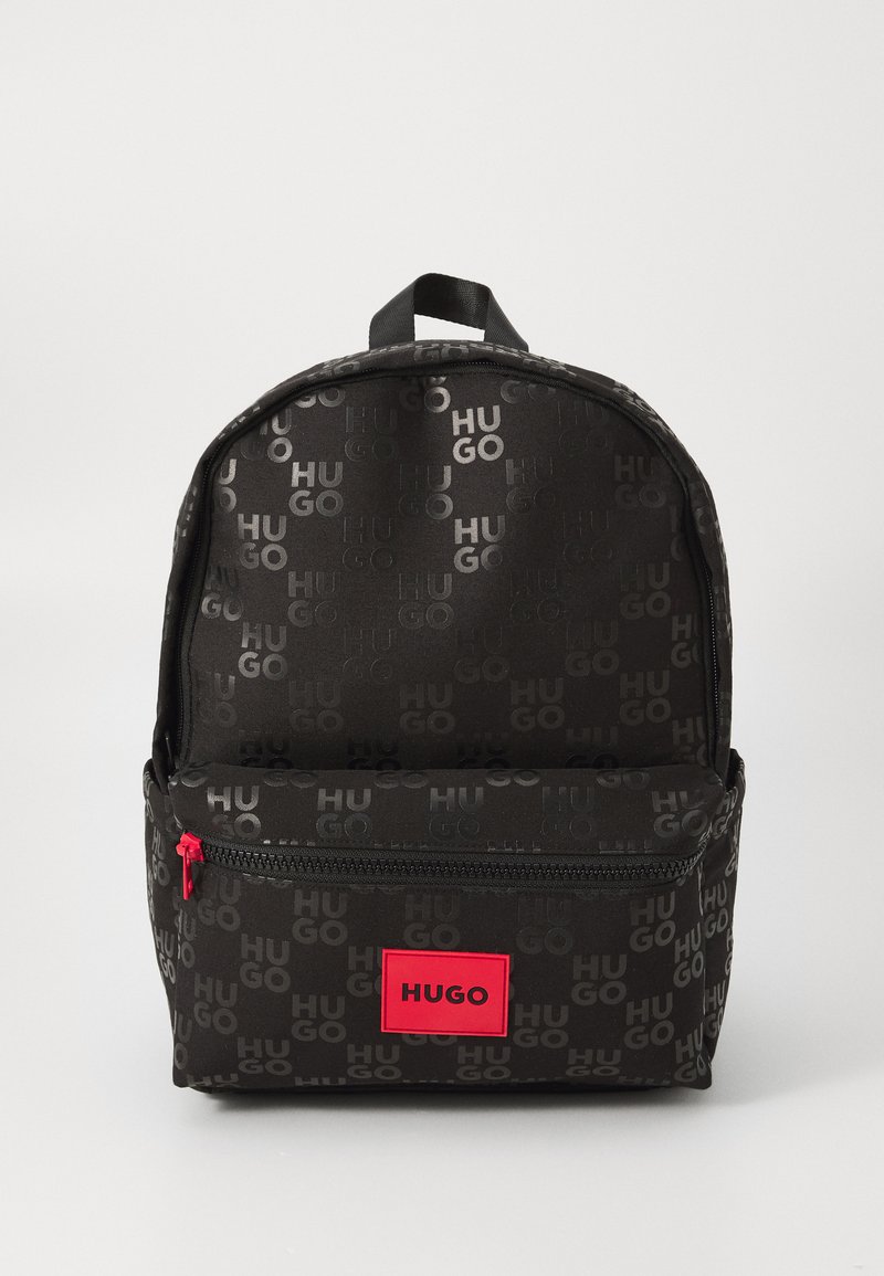 Mochila preta com um padrão sutil de repetição da marca "HUGO". Bolso frontal com fecho éclair e ferragens em vermelho brilhante, além de rótulo do logótipo.