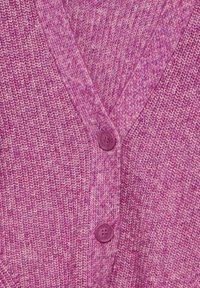 Stickad cardigan i ett flerfärgat rosa tyg, med V-ringning och en enda lila knapp som stängningsdetalj. Strukturerad utseende.