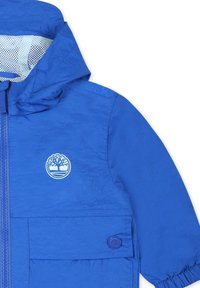 Giacca blu con finitura testurizzata, zip frontale e fodera in rete. Presenta un logo ricamato e polsini elastici con una tasca con bottone.