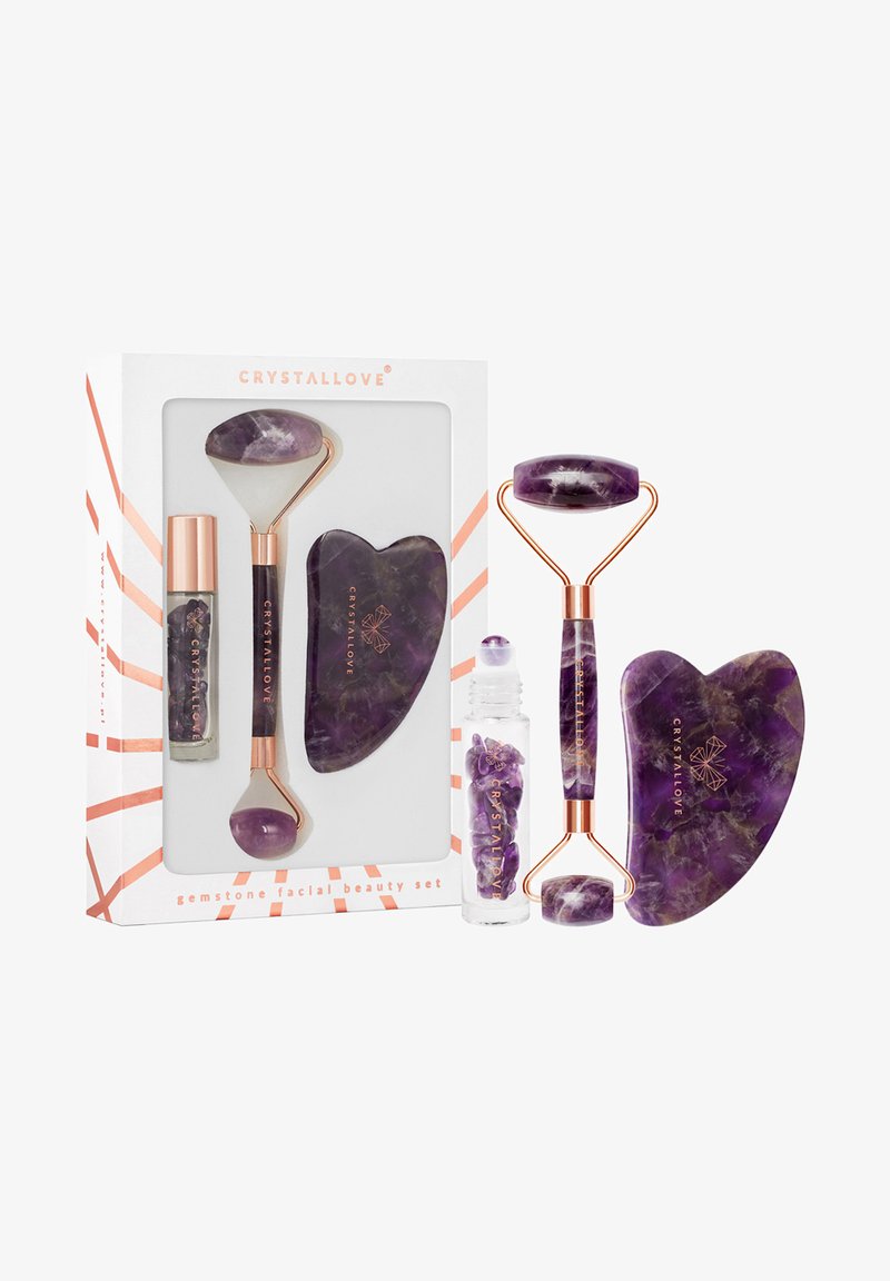 Set di bellezza per il viso con gemme, composto da un rullo in giade viola, uno strumento gua sha a forma di cuore e un rollerball con pezzi di cristallo viola. Accenti in oro rosa.