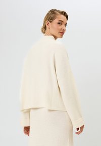 Crème wool-blend cropped trui met verlaagde schouders, brede boorden en een relaxte pasvorm, gecombineerd met een bijpassende rok. Zachte textuur.