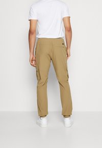Pantalons cargo beiges avec une taille élastique, des poches latérales et une coupe décontractée. Portés avec un t-shirt blanc uni et des baskets blanches.