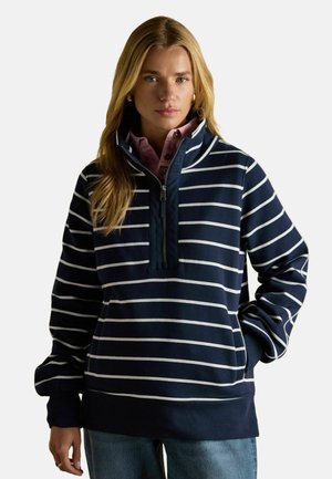 Dunkelblau gestreifter Pullover mit hohem Kragen und halbem Reißverschluss, der weiße horizontale Streifen und locker geschnittene Ärmel aufweist.