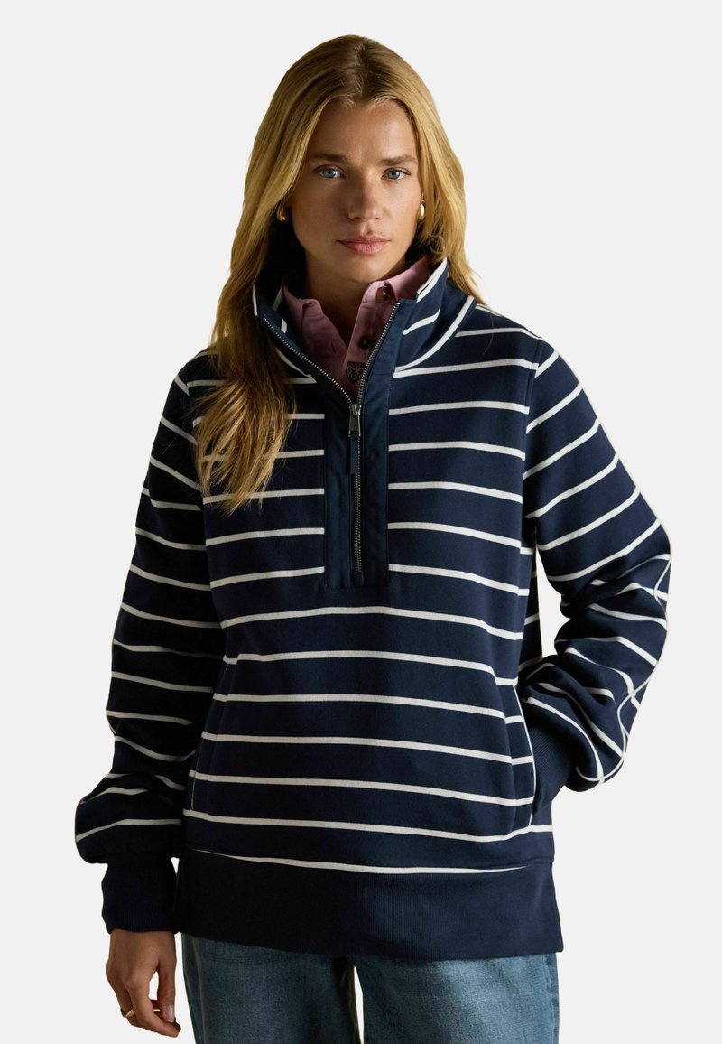 Tumesinine triibuline poolkooti pluus kõrge krae ja poolesipiga, millel on valged horisontaalsed triibud ja vabalt lasuvad varrukad.