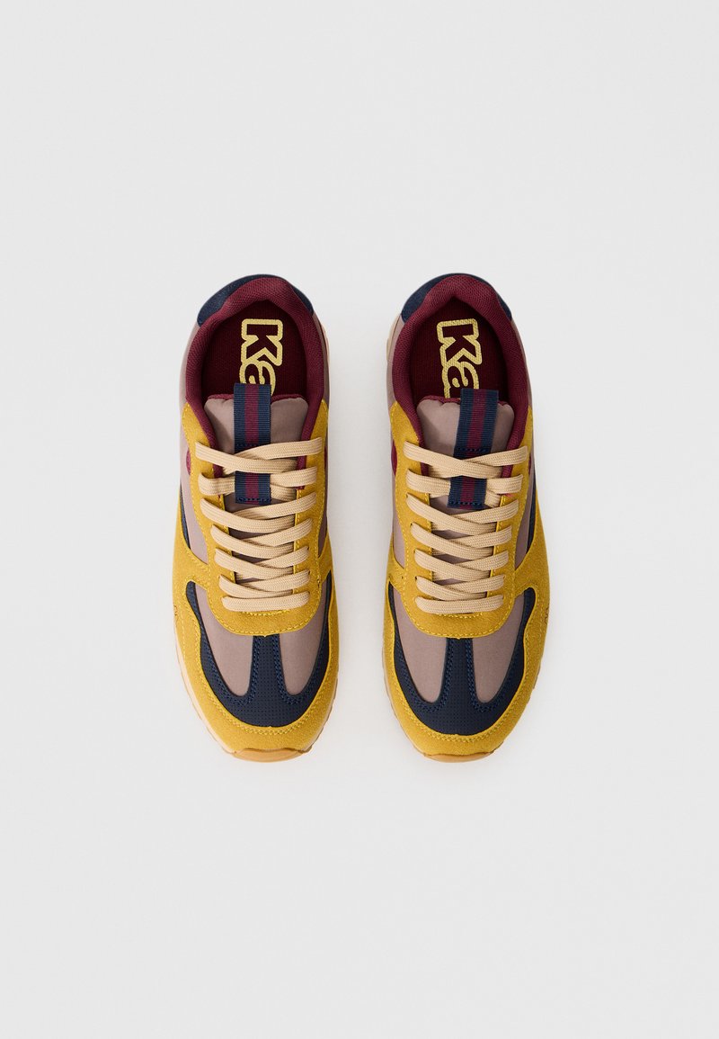 Sneakers con una toma superiore in pelle scamosciata gialla, accenti blu navy, pannelli in rete beige e un collare imbottito color maroon. Suola in gomma testurizzata e lacci beige.