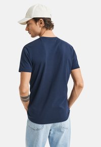 T-shirt blu navy a maniche corte con una texture liscia, scollatura tonda e una vestibilità rilassata, abbinata a jeans azzurri.