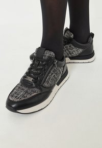Sorte og grå strikkesneakers med læderdetaljer, snørebånd fortil, lynlås i siden og hvide såler. Struktureret stof og sleek design.