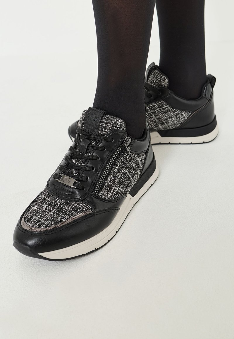 Sorte og grå strikkesneakers med læderdetaljer, snørebånd fortil, lynlås i siden og hvide såler. Struktureret stof og sleek design.