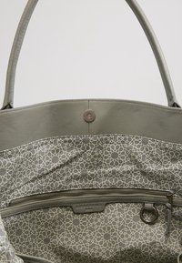 Szara skórzana torba na ramię z wzorzystą tkaniną w geometryczne wzory, kieszonką na zamek i dekoracyjnym okrągłym pierścieniem.