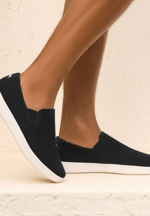 Black slip-on shoes made of breathable mesh material, featuring a white sole and elastic side panels for easy wear.
