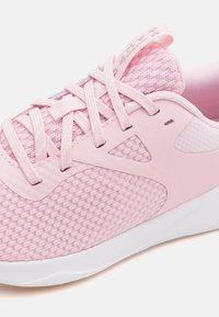 Ljust rosa träningsskor med en texturerad mesh-överdel, släta syntetiska detaljer och platta skosnören. Sulan är vit med en lätt kurva.