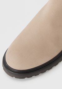 Stivale alla caviglia in pelle beige con una texture liscia, punta tonda e suola in gomma nera con dettagli in rilievo.