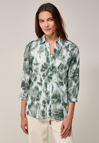 Grön och blå mönstrad blus med krage, 3/4 ärmar och lätt tyg. Har en knäppning framtill och uppvikta ärmslut.