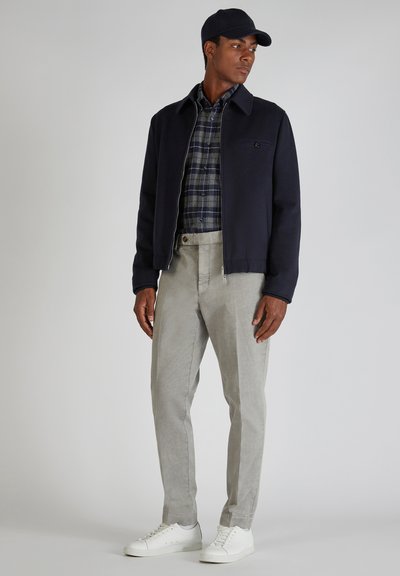 Marineblauer Blazer mit Kragen, karierter Hemd, hellgraue Hose und weiße Sneakers. Slim-Fit mit Reißverschluss, minimaler Hardware und ohne Muster.