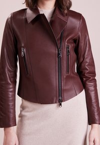 Burgunderfarbene, kurze Lederjacke mit Reverskragen, frontalem Reißverschluss und vier Reißverschlusstaschen. Glatte Textur mit taillierten Ärmeln.