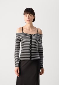 Top rayé noir et blanc à épaules dénudées avec des manches longues, présentant une fermeture à boutons sur le devant et une bordure noire. Texture de tissu lisse.