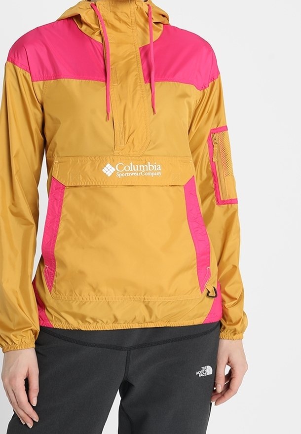 Giacca leggera con cappuccio gialla e rosa, dotata di tasca frontale, dettagli in rete sulla manica, polsini elastici e cordino regolabile.