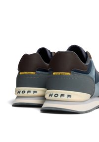 Zapatillas azul y gris con acentos marrones, que presentan un material superior liso, una suela acolchada y un logo elevado en el talón.