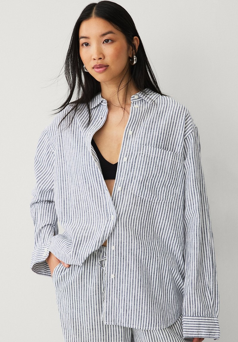 Camisa de cuadros en algodón azul y blanco, de corte holgado con un bolsillo en el pecho y un dobladillo redondeado, combinada con pantalones a juego.