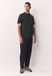 Tumehelist värvi lühikeste varrukatega t-särk, mis on kombineeritud lahtiste mustade pükstega ja mitmevärviliste spordijalatsitega, millel on logo. Lihtne, tasapinnaline disain.