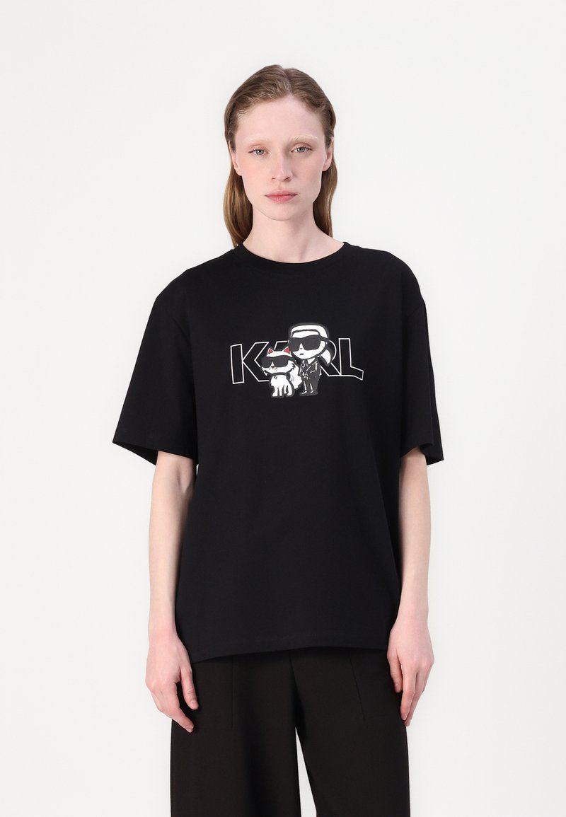 Black cotton t-shirt with loose fit, featuring a graphic print of stylized characters and "KARL" text in contrasting white. Short sleeves.