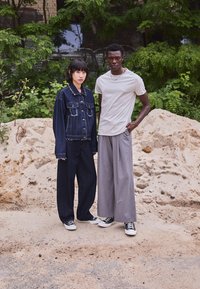 Denimjakke med frynser og lommer, sammen med vide jeans; grå bomulls t-skjorte og løse grå bukser, begge med joggesko.