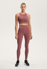 Csíkozott, testhezálló sportmelltartó és magas derekú leggings, tompa rózsaszínben. Sima textúra varrással és fekete sportcipőkkel.