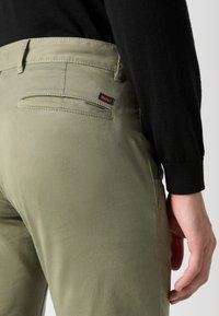 Olivgrön byxor med slim fit, slät textur, bakfickdetalj och en liten svart och orange logotagg.