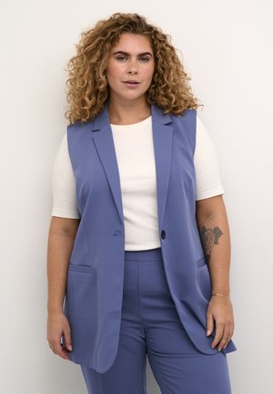 Light blue sleeveless blazer with a notch lapel, front pockets, and a single button closure, worn over a white ribbed shirt.