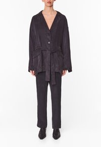 Conjunto de loungewear de color púrpura oscuro hecho de una tela suave. Chaqueta de manga larga con cierre de botón y cinturón, acompañada de pantalones rectos.