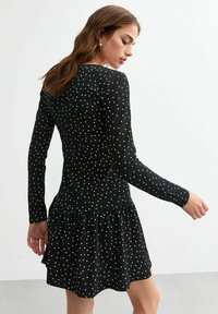 Vestido negro de manga larga con lunares blancos, que presenta un corsé ajustado y una falda acampanada. Fabricado con una tela texturizada.